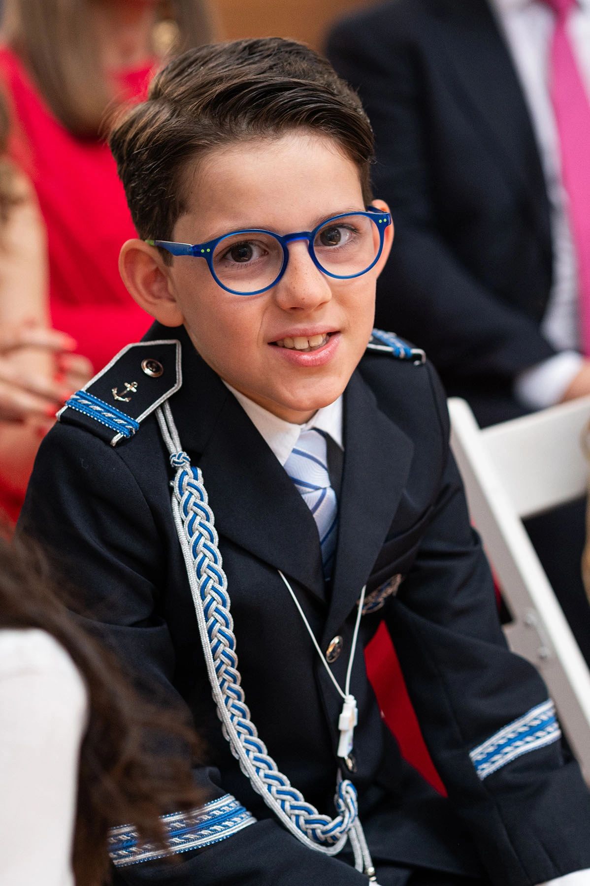 Young boy dressed in a formal navy uniform with blue glasses.