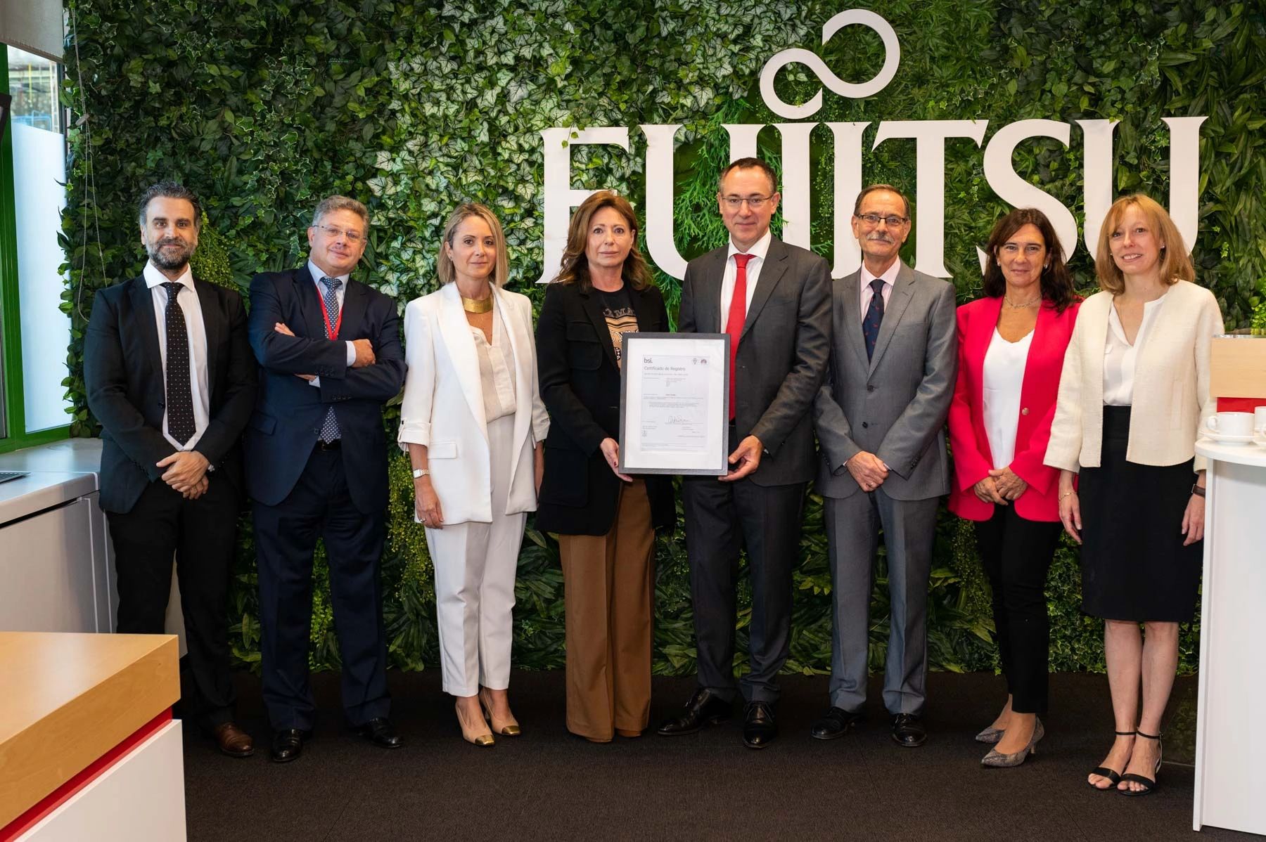 Group of professionals posing with a certificate in front of a Fujitsu logo and green wall.