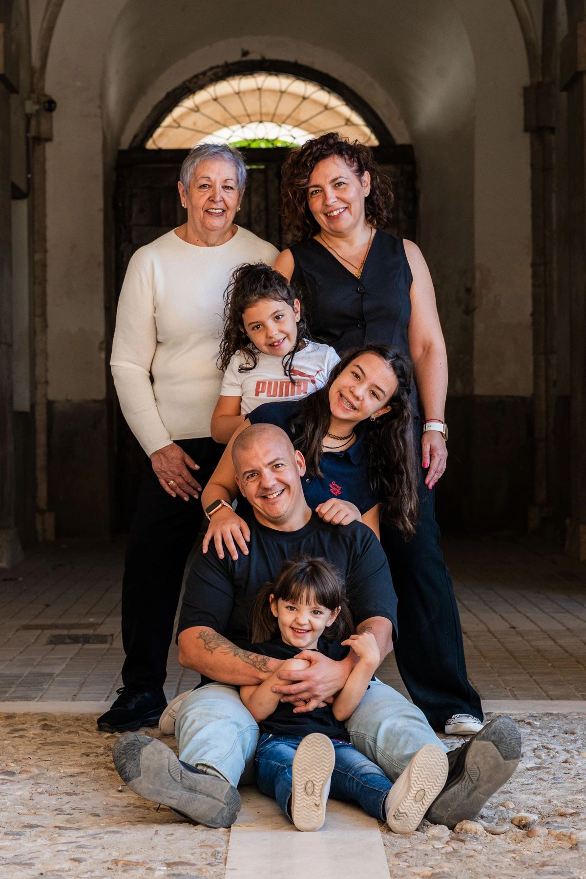 A joyful multi-generational family posing together in a warmly lit archway.