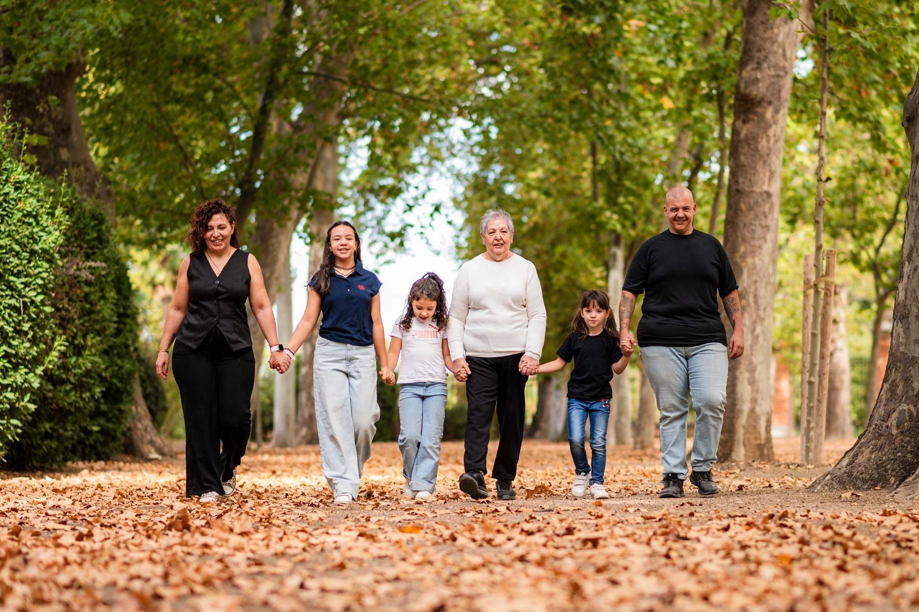 A multigenerational family holding hands and walking through a leafy park.