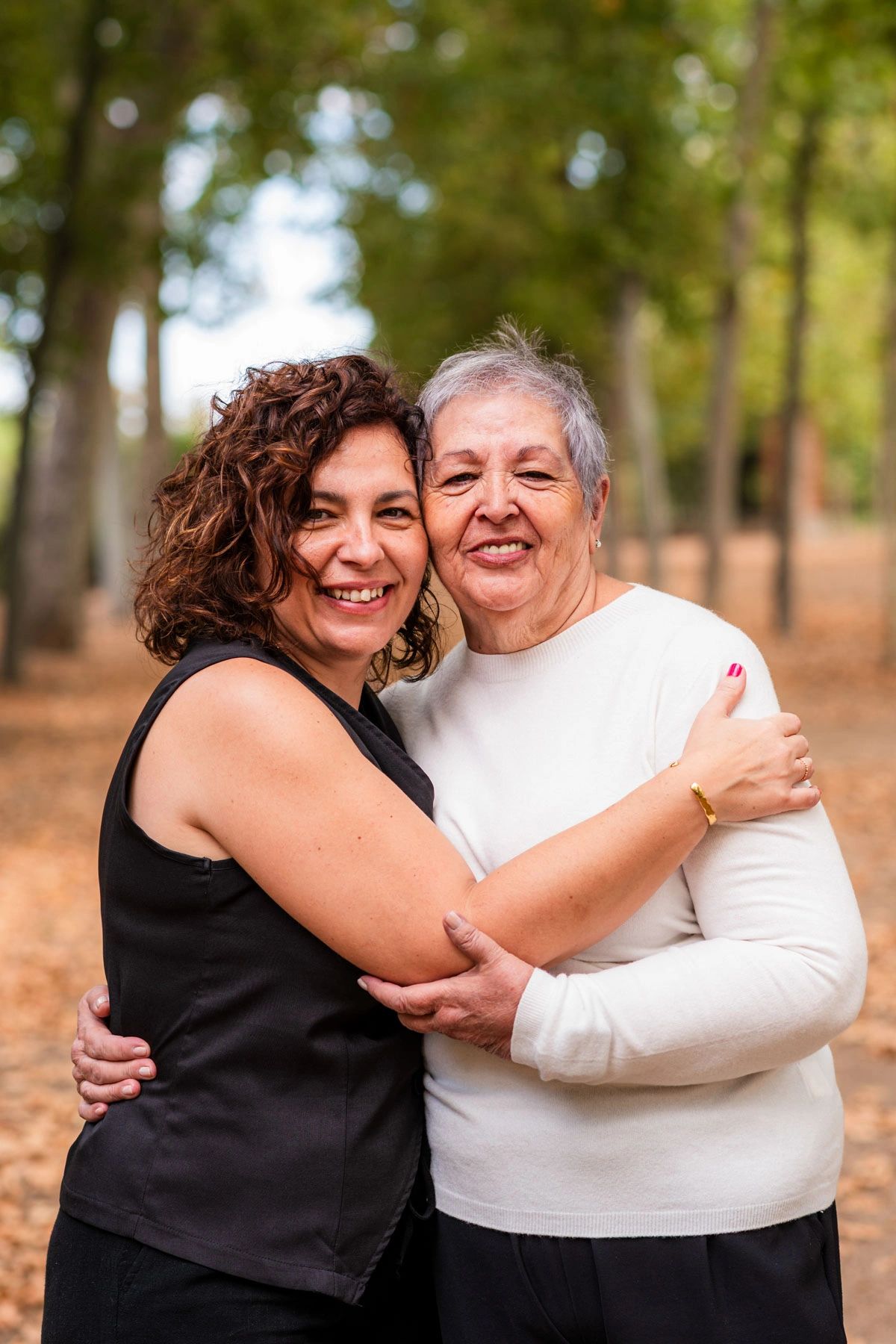 Two women sharing a warm embrace outdoors in a forest setting.