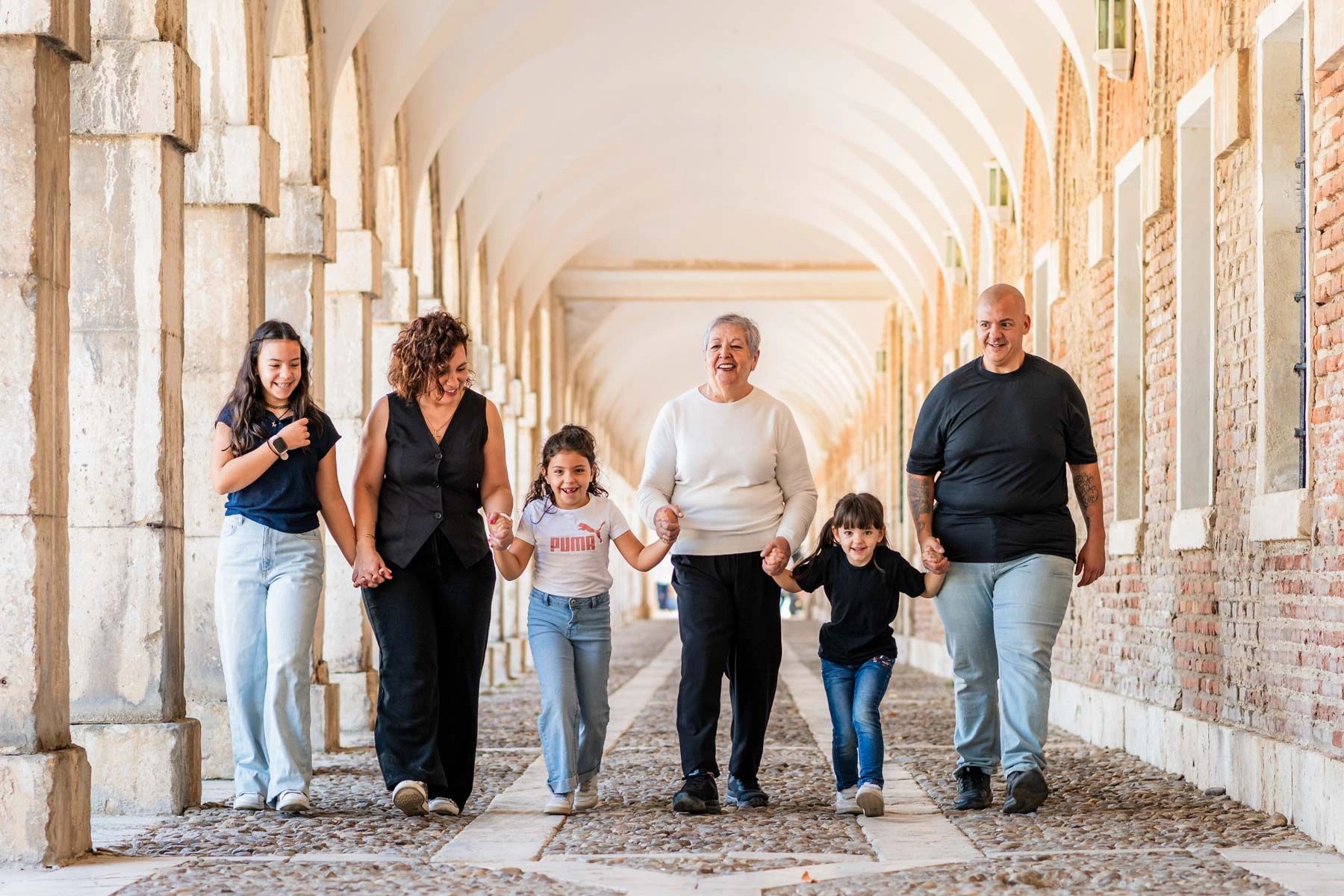 A joyful multi-generational family walking hand in hand under an arched corridor.