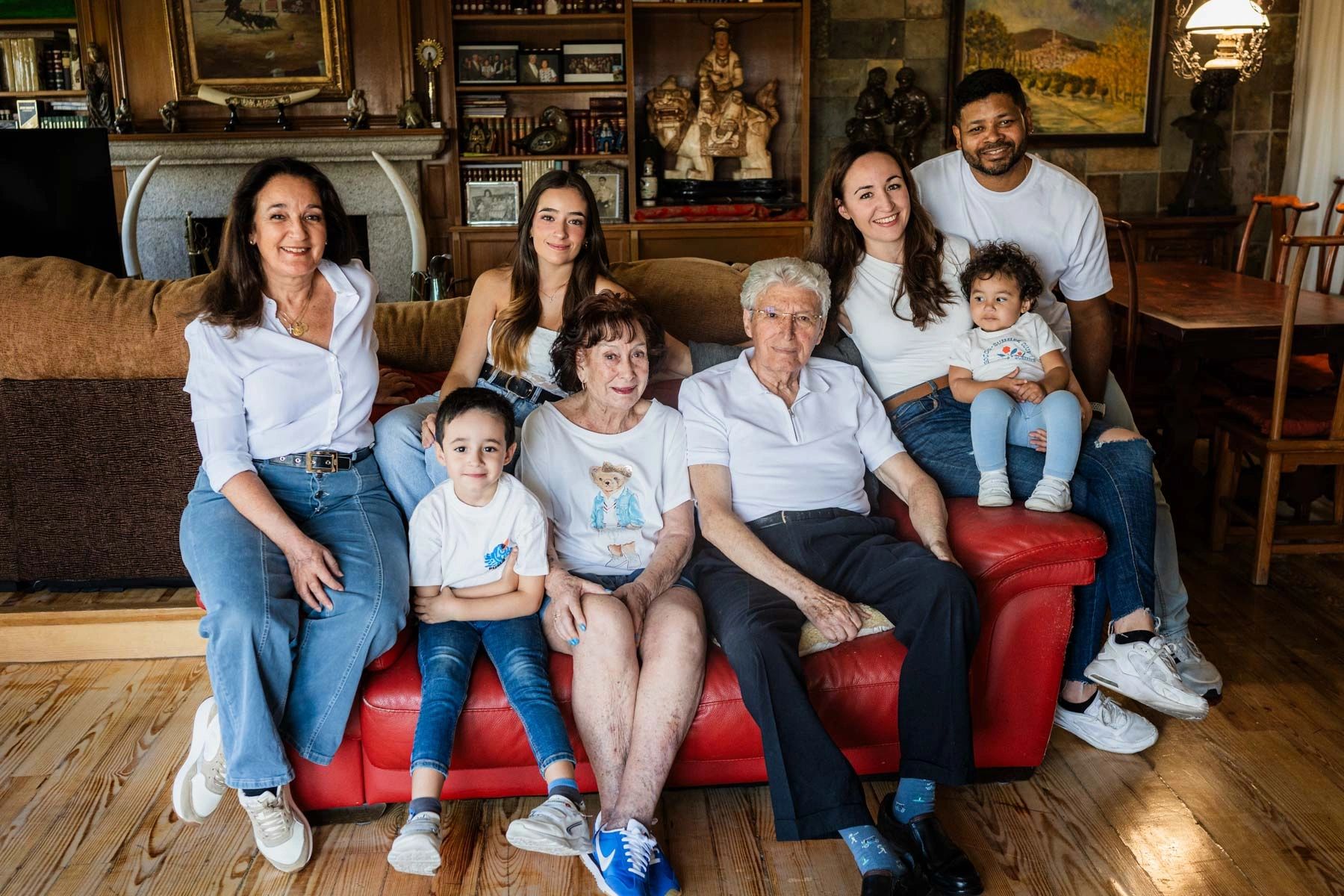 A multi-generational family smiling together on a red couch in a cozy living room.