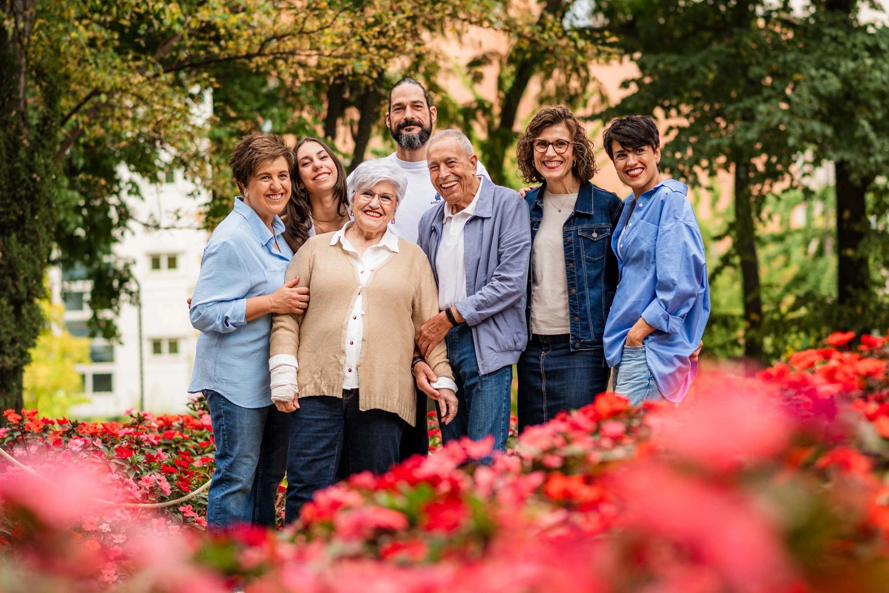 A happy multigenerational family posing outdoors surrounded by vibrant flowers.