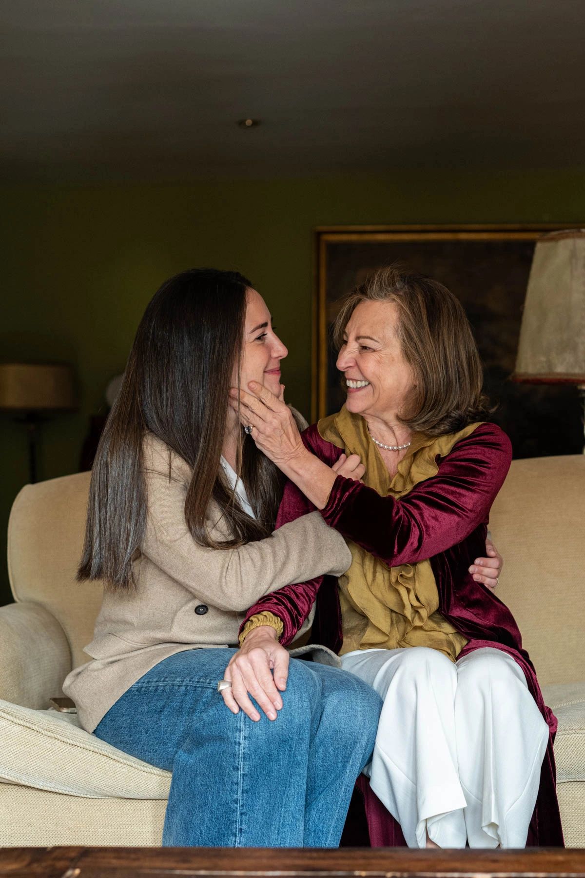 A joyful older woman and younger woman share a warm moment on a couch.