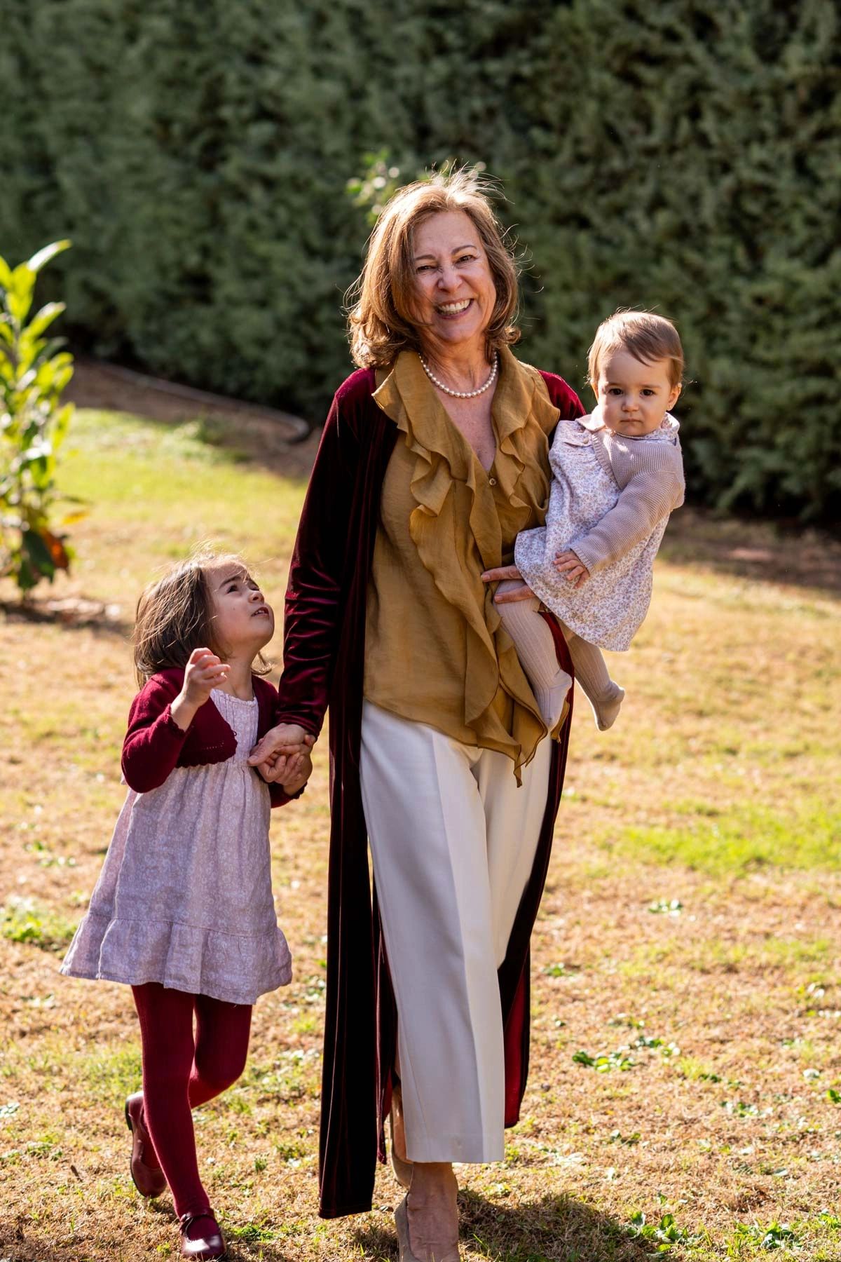 Smiling grandmother walks outside holding hands with her two young granddaughters.