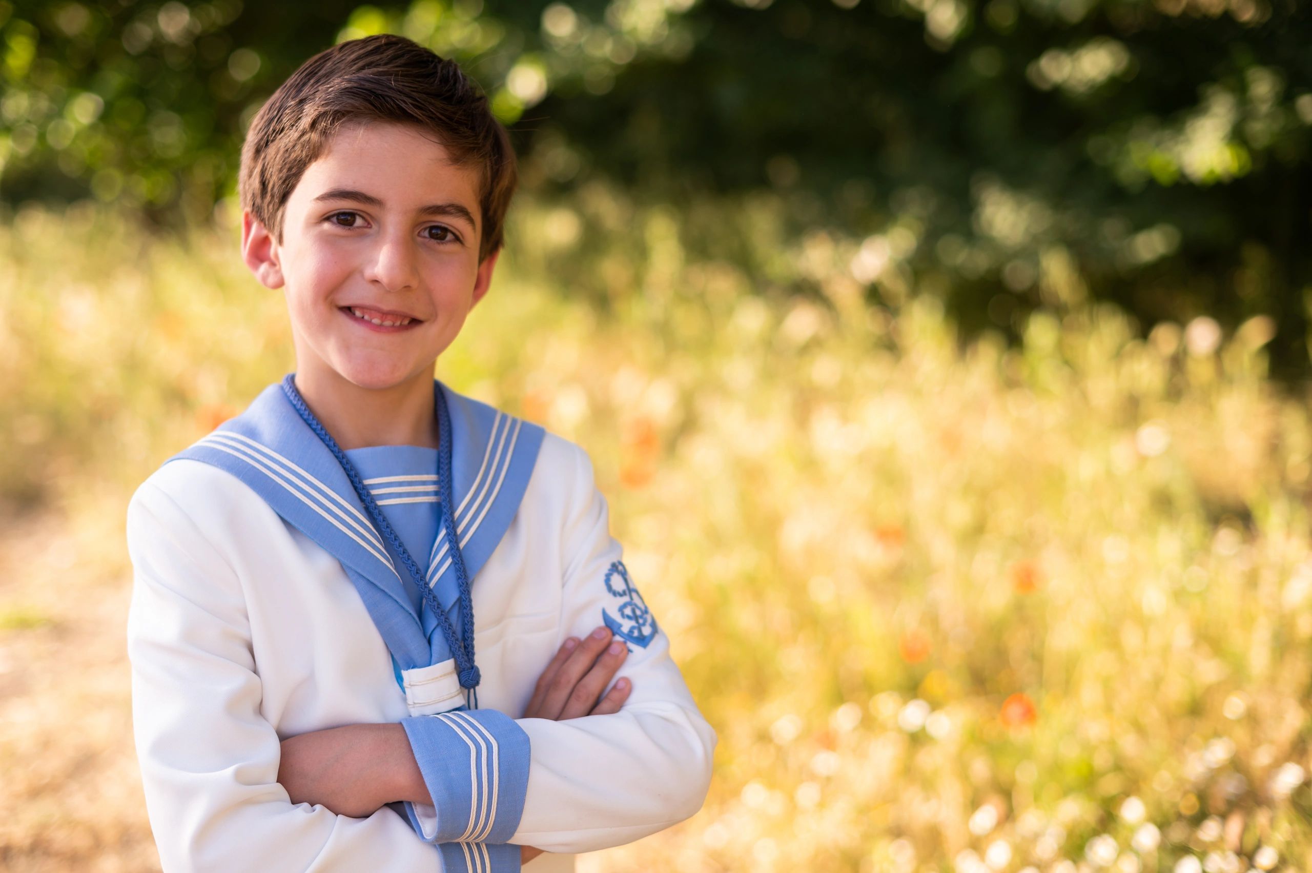 Smiling boy in a white and blue sailor suit outdoors.