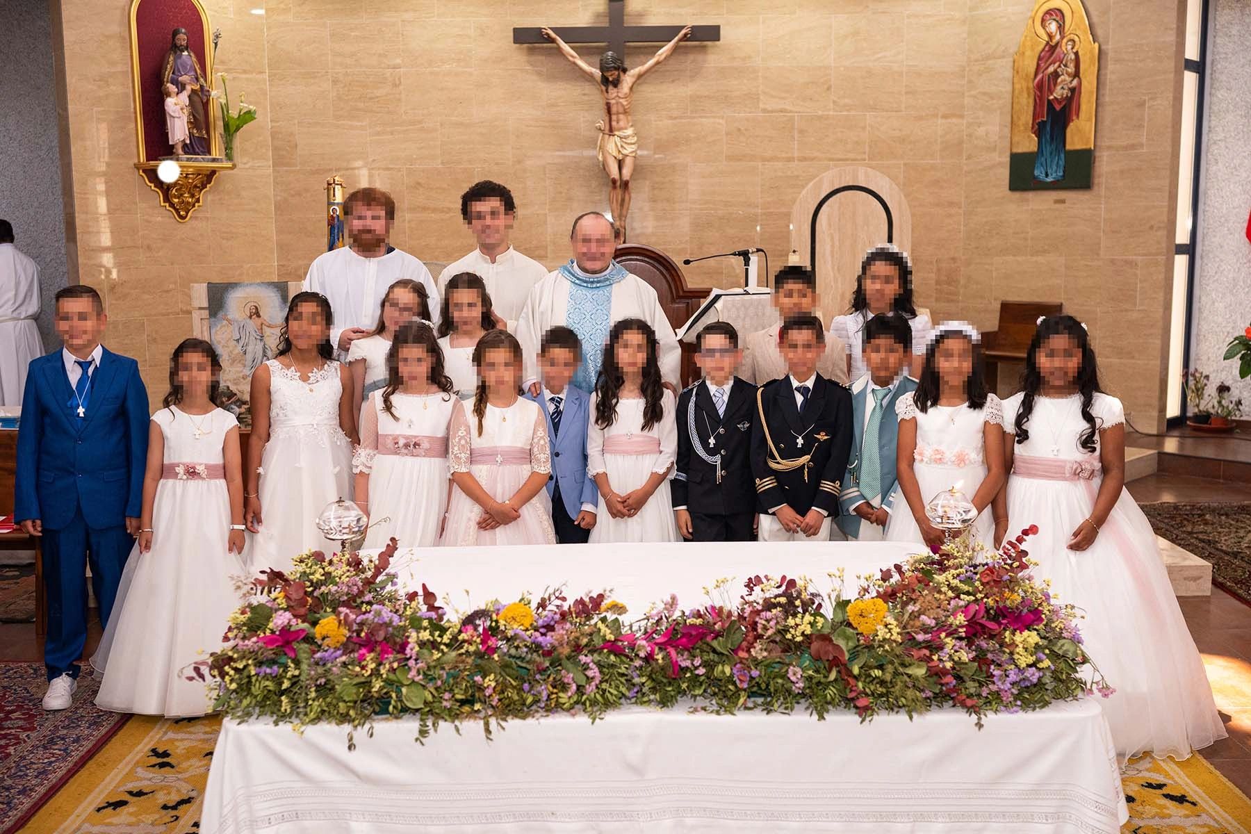 Group photo of children and clergy in a church, dressed for a religious ceremony.