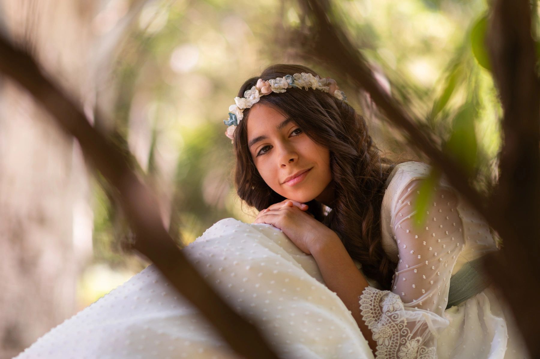 Young woman in a delicate white dress with floral headband resting outdoors.