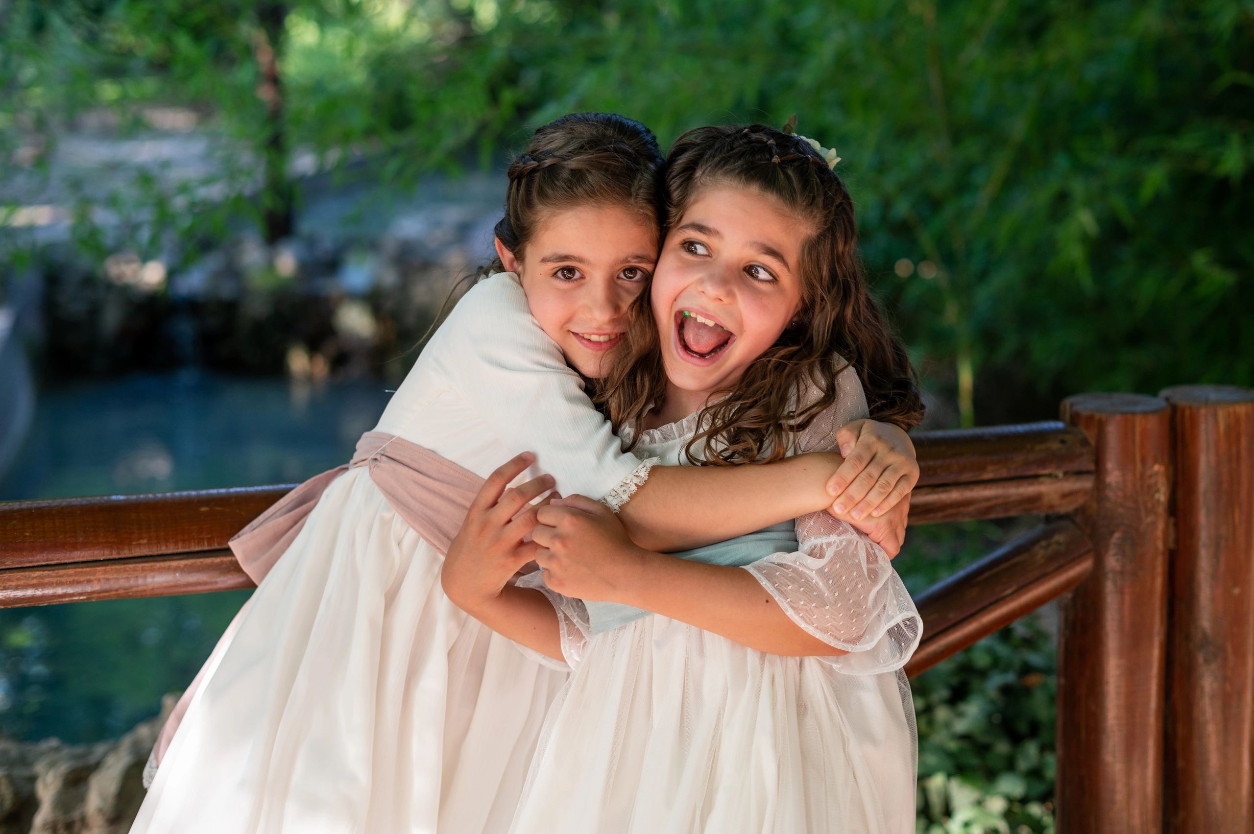 Two joyful young girls hugging on a wooden bench outdoors.