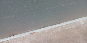 A close-up of a concrete curb and pavement with a wet surface.