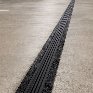 Expansion joint on a concrete surface filled with black material.