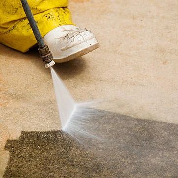 Person power washing a dirty concrete surface.