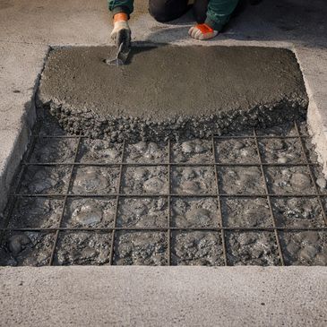 Worker smoothing wet concrete over rebar grid for pavement repair.