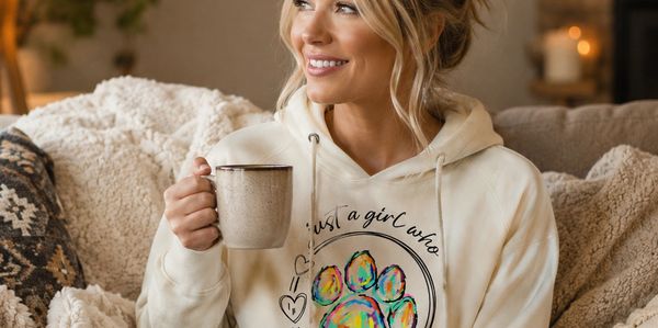 Woman in cozy hoodie holding a mug and smiling warmly.