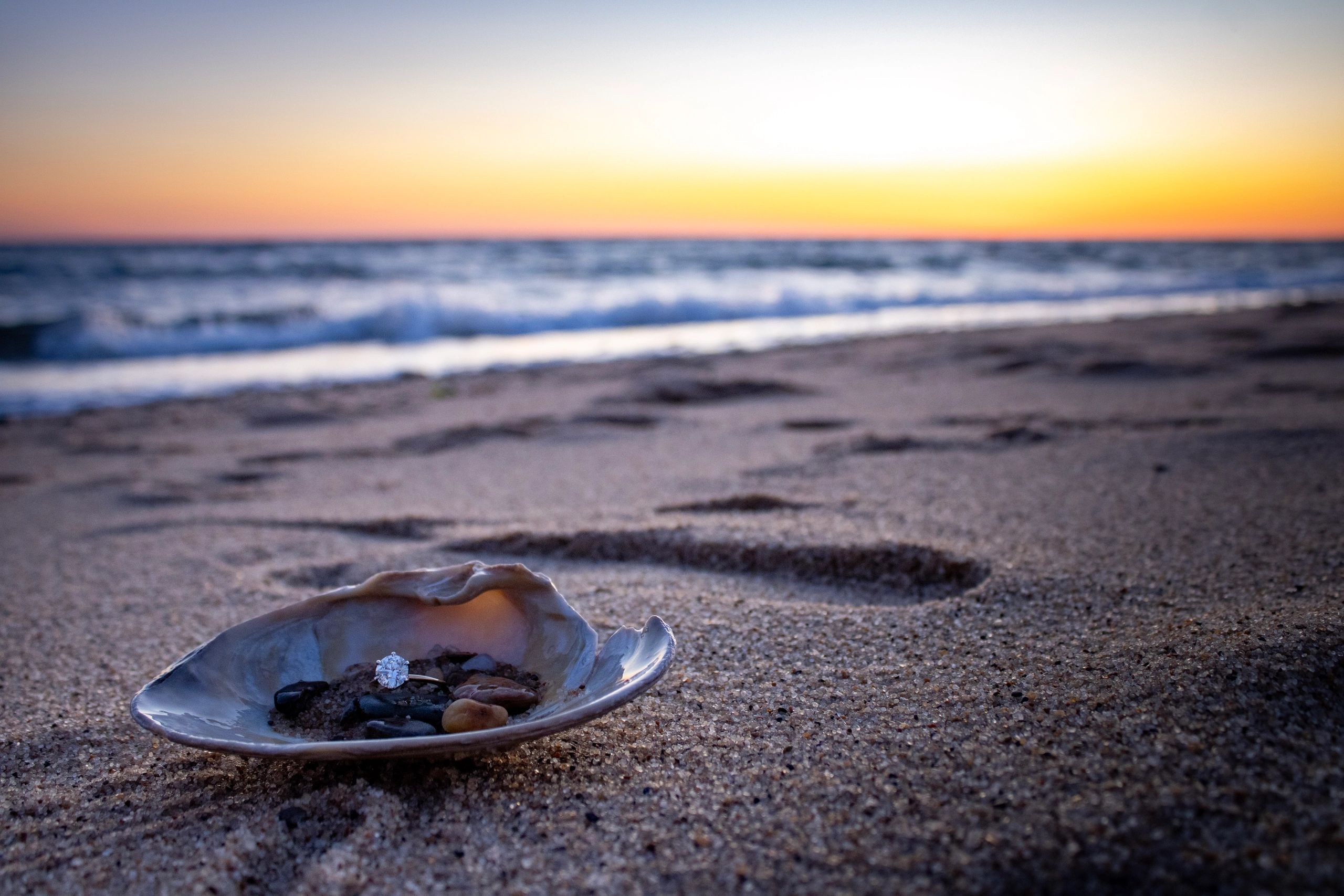 Romantic beach proposal detail photo showing an engagement ring  in a seashell on the sand at sunset