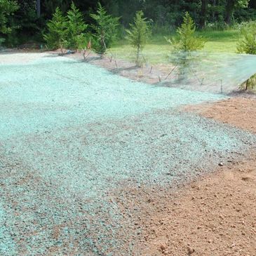 Person spraying blue-green hydroseed mixture on soil for grass planting.