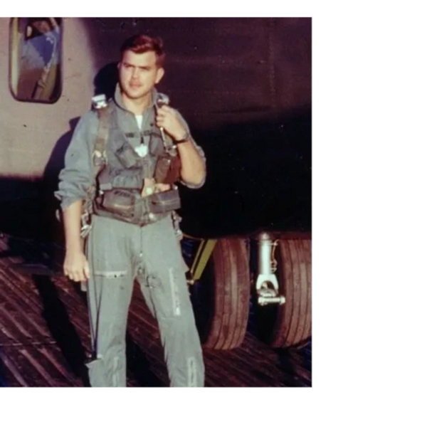 Young pilot in flight suit standing by aircraft wheel, adjusting gear.