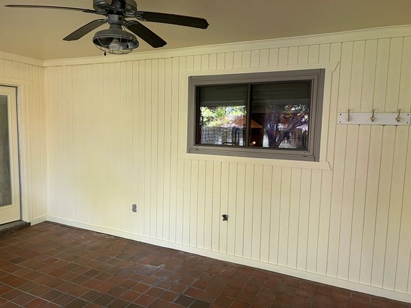Empty room with cream vertical panel walls, terracotta tile floor, and ceiling fan.