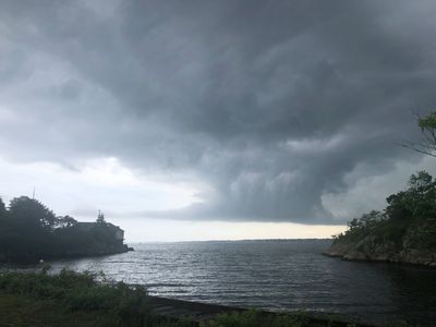 Dark storm clouds gather over a calm lake between tree-lined shores.