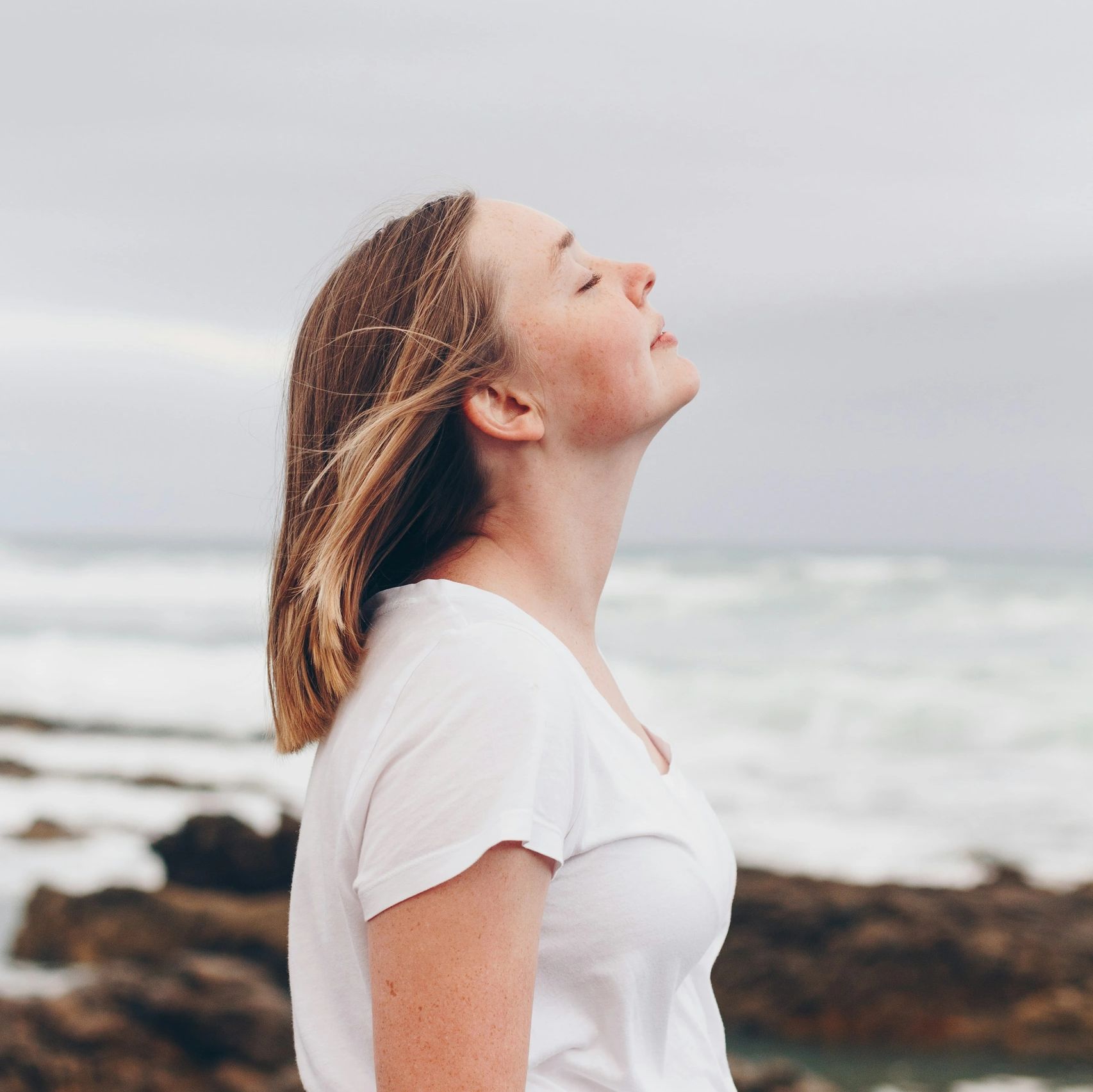 Woman enjoying a peaceful moment by the ocean, eyes closed and face lifted.