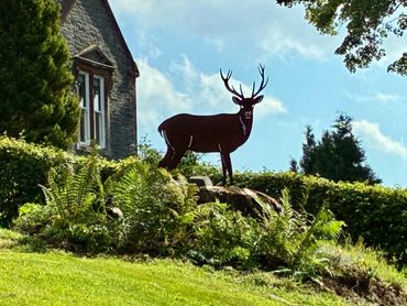 Silhouette of a deer statue on a grassy hill beside a stone building.