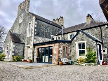 A traditional stone house with multiple chimneys and a gravel driveway.