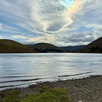 Serene lake with rippling water surrounded by rolling hills under a cloudy sky.