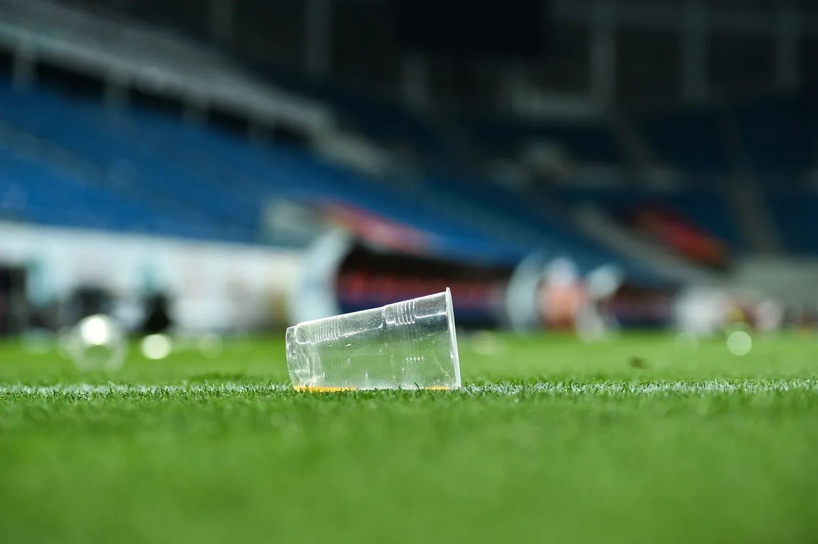 A plastic cup lies on a grassy sports field near the sidelines.