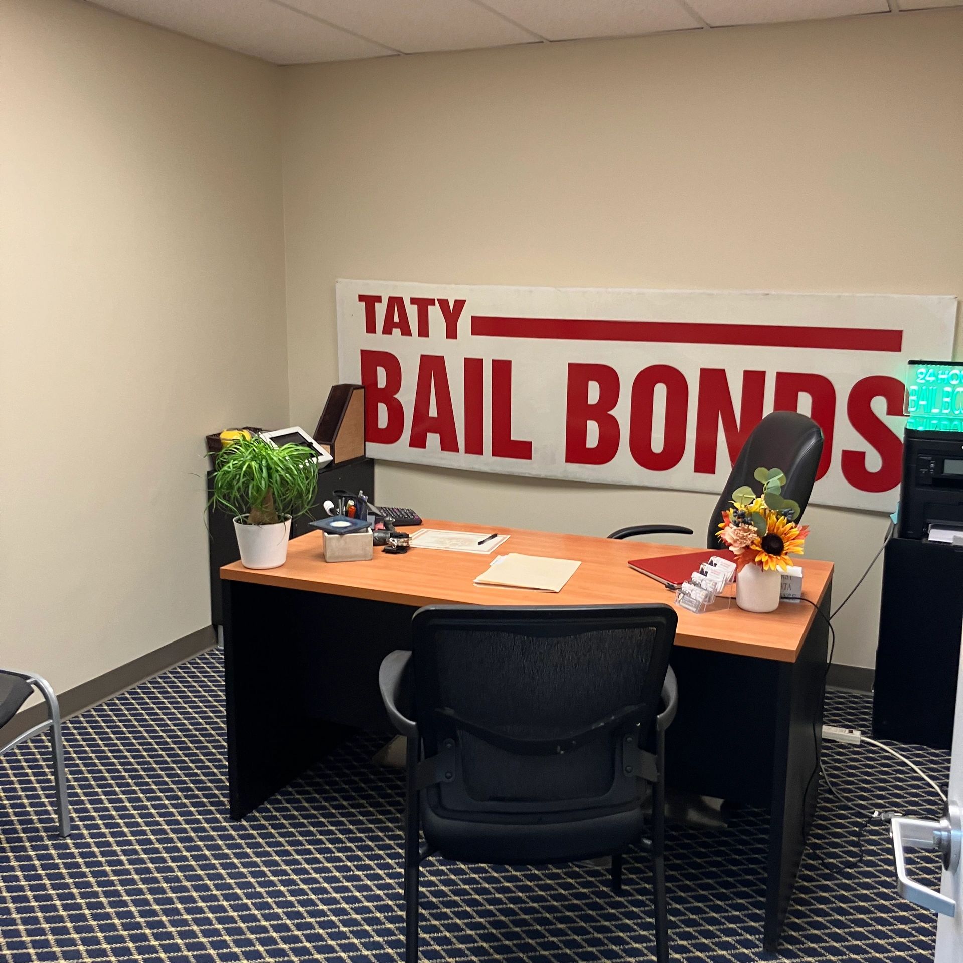 Office desk with a 'Taty Bail Bonds' sign and decorative plants.