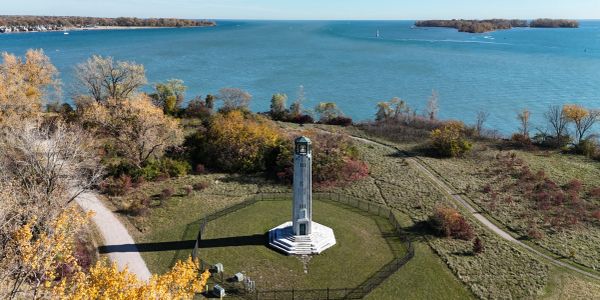 Tall monument near a large body of water with autumn trees.