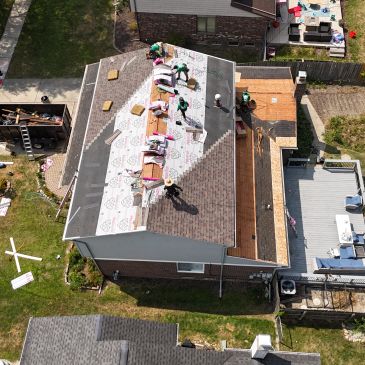Workers installing roofing shingles on a house from an aerial view.