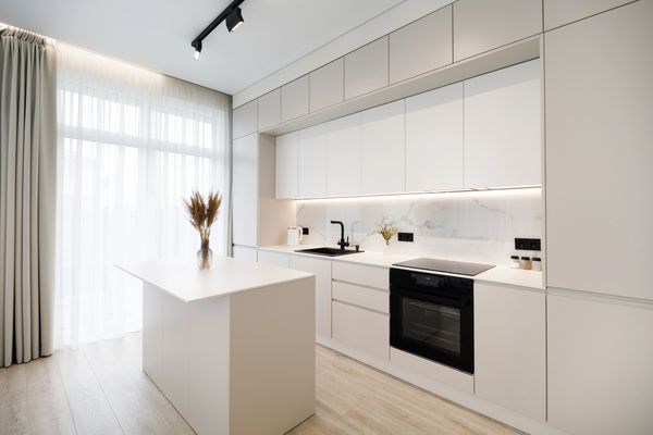 Modern kitchen featuring white cabinetry, marble backsplash, black sink, and an island with a vase