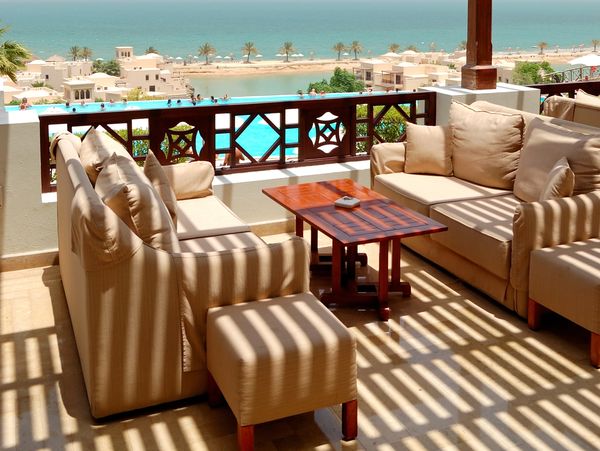 A sunny balcony with plush beige seating, a wooden table