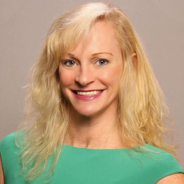 Smiling blonde woman in a green top against a neutral background.