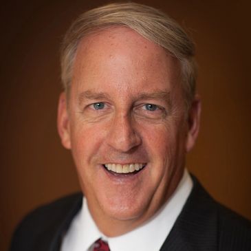 Smiling middle-aged man in a suit and tie against a brown background.