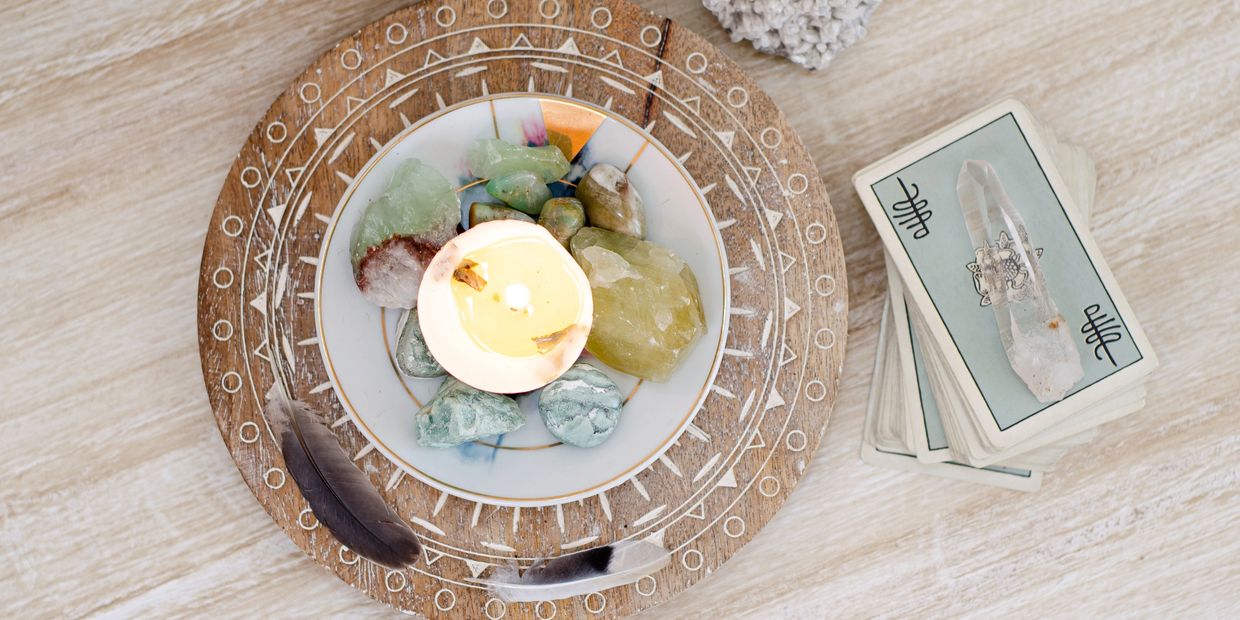 A bowl of crystals with a lit candle, feathers, and tarot cards with a quartz crystal.