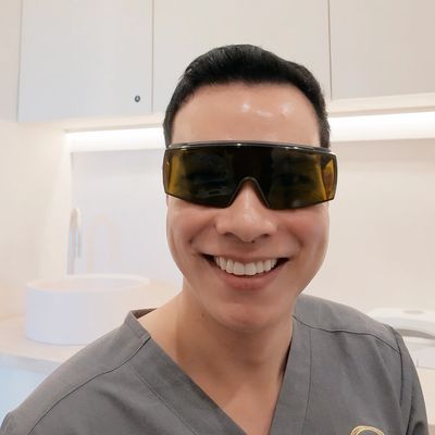 MOSO Clinic technician smiling in grey scrubs and laser glasses at the Bowen Hills clinic.