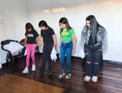 Four girls practicing dance steps indoors on a wooden floor.