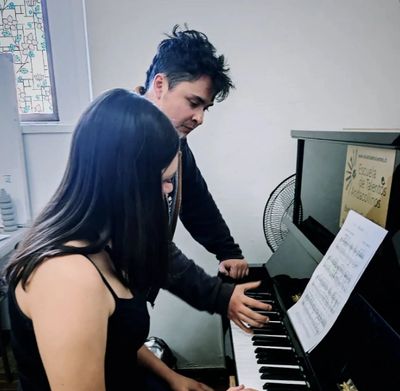 A man teaching a woman to play piano indoors with sheet music.