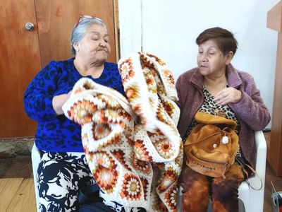 Two elderly women examining a crocheted blanket indoors.