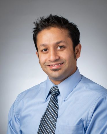 Man in blue shirt and striped tie smiling.