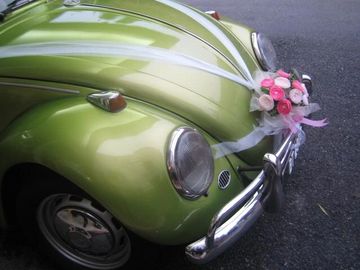 A green Volkswagon beetle with wedding flowers and decorations attached to the front of the car.