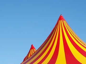 Two brightly coloured red and yellow striped circus tents. The sky is a bright blue and clear.