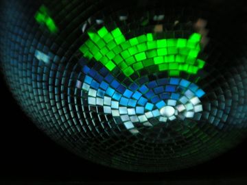 A close up of a disco ball with reflections of green and blue.