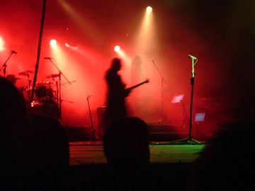 A blurred image of an artist on stage. The microphone is in focus and the stage lighting is in red.