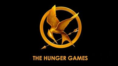 Golden Mockingjay pin with arrow and text The Hunger Games on black background.