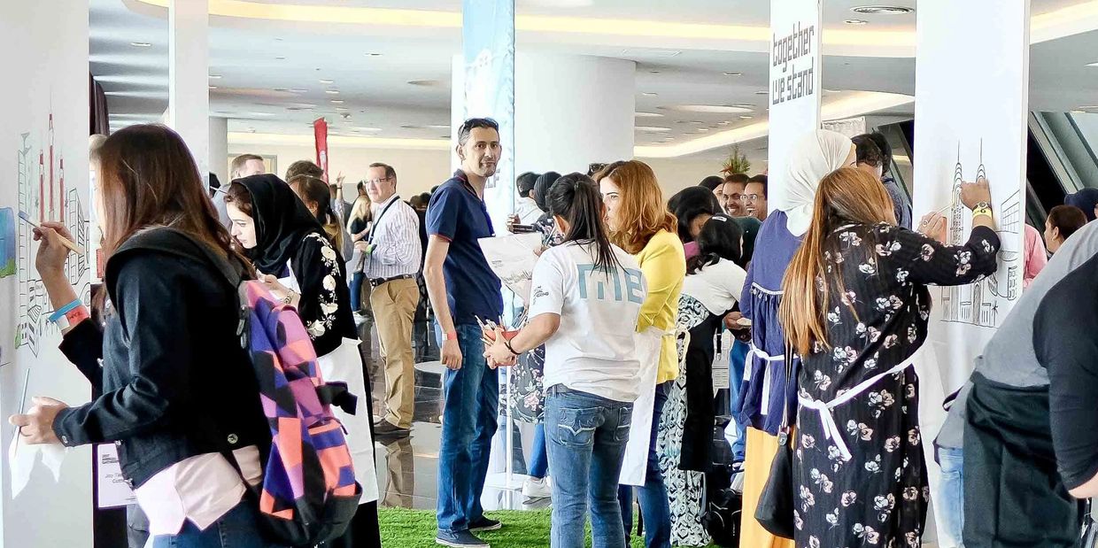 People painting on white panels at an indoor event with green carpet.