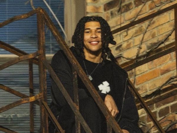 A young man with dreadlocks smiling on outdoor stairs.