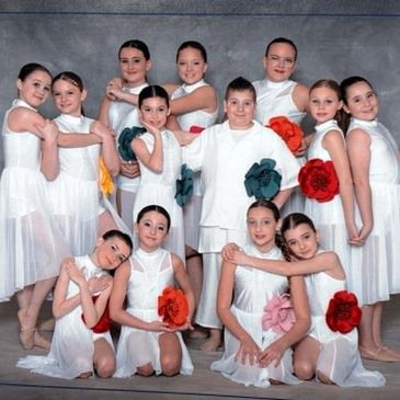 Groupe d'enfants en costume de danse blanche posant avec des fleurs colorées.